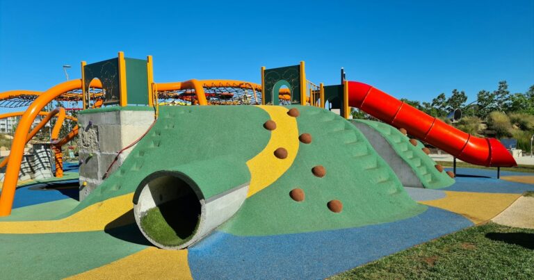 Colorful children’s playground with a climbing hill, tunnel and red tube slide under a blue sky