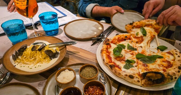 Pizza with basil and a plate of pasta shared on a restaurant table