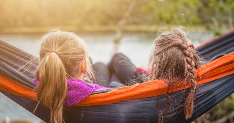 Two kids relaxing together in a hammock beside a lake on a summer afternoon