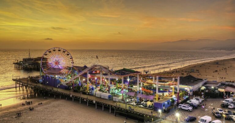 Aerial view of the Santa Monica Pier and its Ferris wheel lit up at sunset in Los Angeles